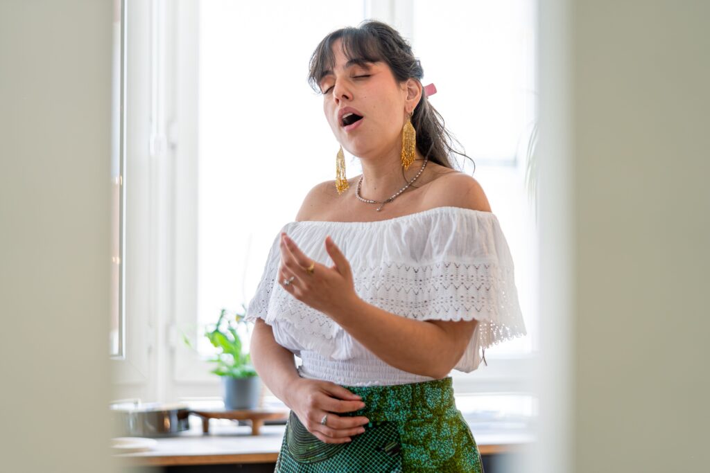 pexels photo 26835531 26835531 A young woman passionately singing indoors, wearing a white top with green skirt.